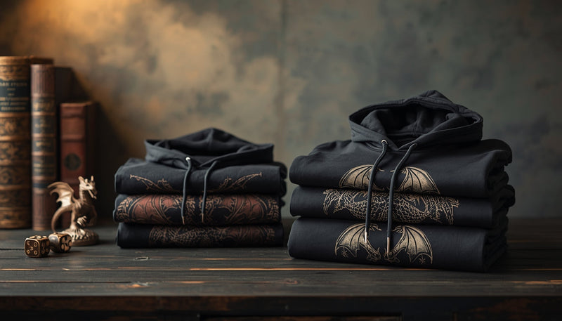 Folded dragon graphic hoodies stacked on a wooden table with subtle fantasy props under warm cinematic lighting.