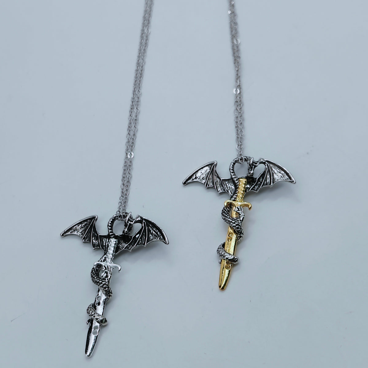 Dragon sword pendant necklaces in silver and gold finishes laid flat