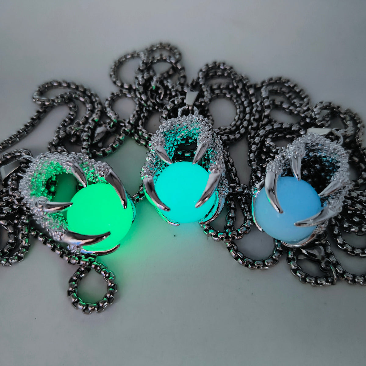 Three silver-tone dragon claw necklaces holding glowing orbs in green, turquoise and blue, with matching alloy chains.