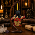Lisa Parker black cat gift box Christmas ornament displayed on a wooden stand in a warm fantasy collector's study.