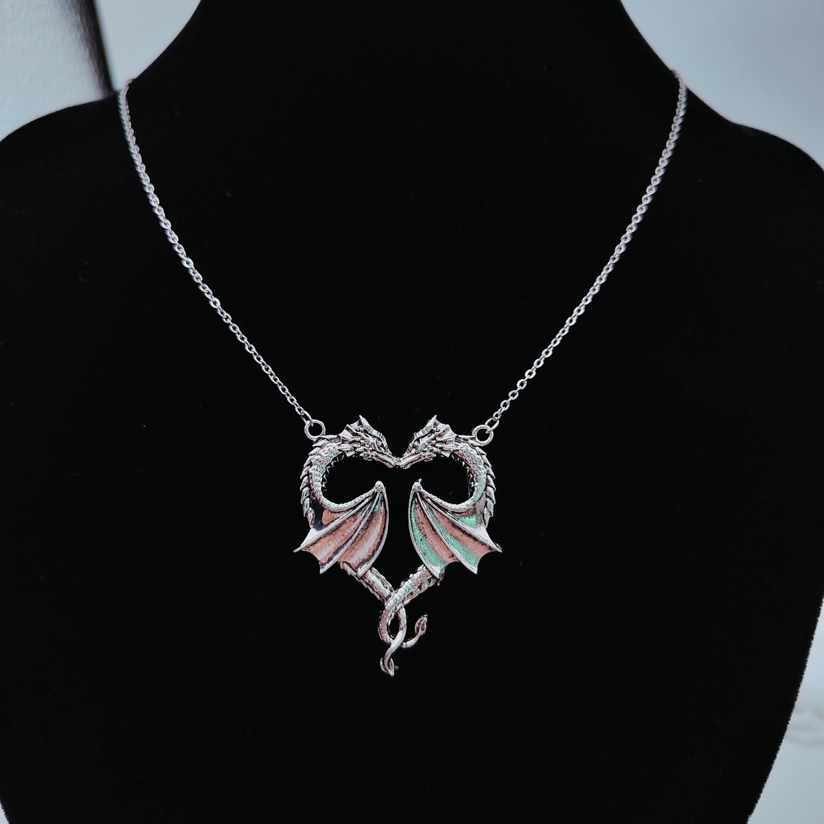 Silver twin dragon heart pendant and chain displayed on black jewellery bust
