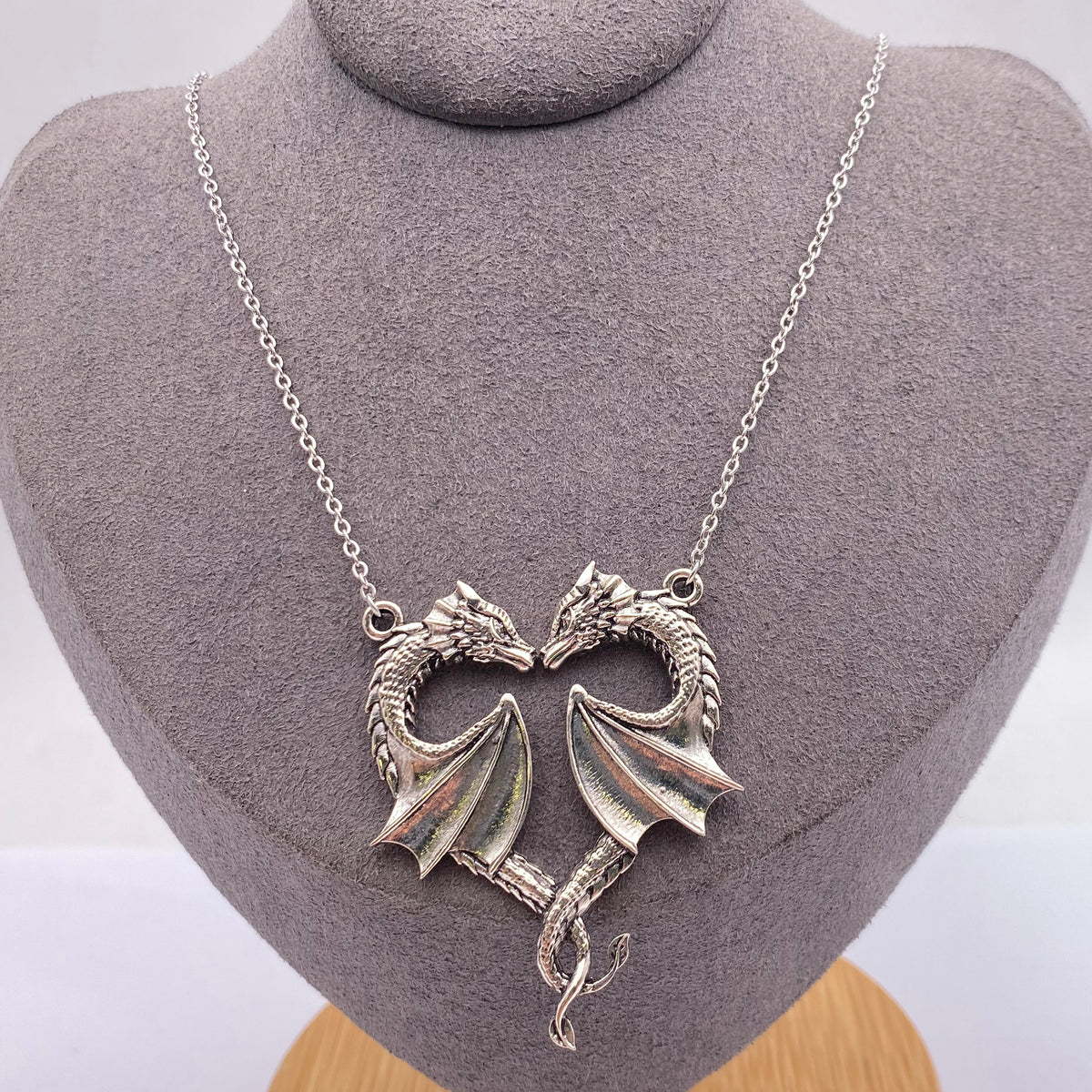 Silver twin dragon heart necklace displayed on grey jewellery bust