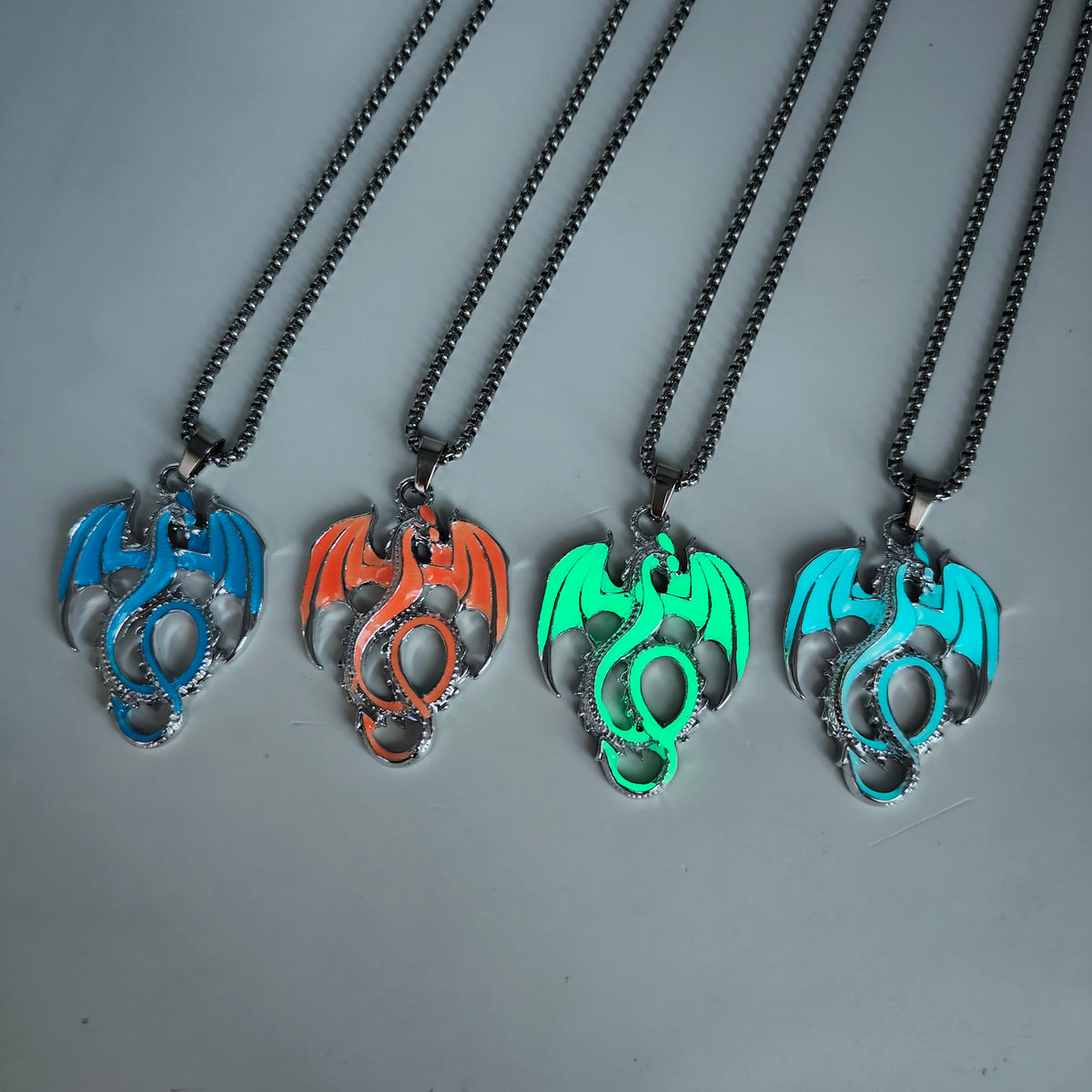 Four glow in the dark Wyvern Dragon necklaces in blue, flame orange, green and light blue